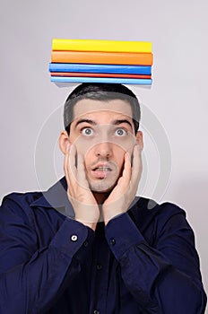 Surprised student holding a pile of books on his head.