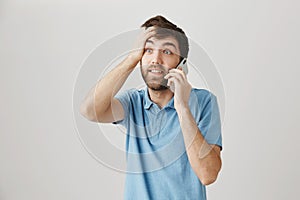 Surprised and stunned european guy talking on smartphone, punching forehead with hand as if remembering something