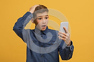 Surprised teen boy staring at smartphone screen and opening mouth in shock