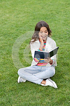 surprised teen child read book sitting on grass. reading book. reader girl with book outdoor