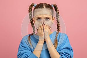 Surprised teen covering mouth with hands on pink background