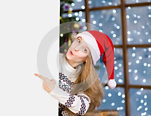 Surprised teen girl in red christmas hat peeking and pointing at empty board