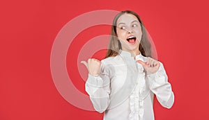 surprised teen girl in white shirt pointing finger on red background copy space, directing