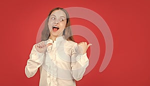 surprised teen girl in white shirt pointing finger on red background copy space, directing