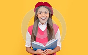 surprised teen school girl in french beret reading book on yellow background, happiness