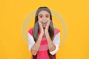 surprised teen school girl smiling with long hair on yellow background, surprise