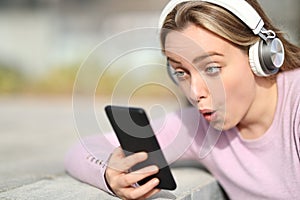 Surprised teenage girl checking phone audio content