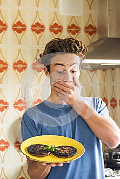 Surprised teenager after brned two hamburger cooked in the kitchen at home - young boy do chef and mistakes.- funny people real