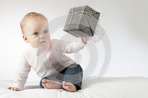 Surprised toddler boy with a present in the hand. Thoughtful infant kid gives a present. Open-eyed baby boy.