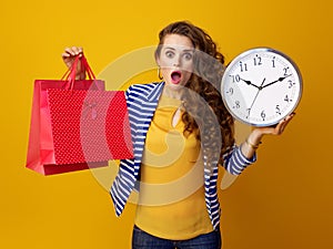 Surprised trendy woman showing clock and red shopping bags