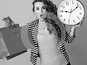 Surprised trendy woman showing clock and shopping bags