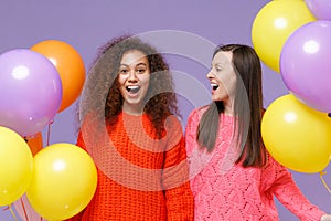 Surprised two european african american women friends in knitted sweaters isolated on violet purple background. Birthday