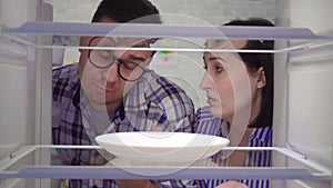 Surprised and upset a married couple looks into an empty refrigerator