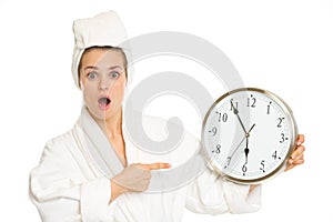 Surprised woman in bathrobe pointing on clock