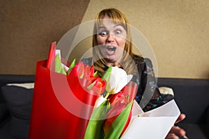 Surprised woman. Beautiful middle-aged blonde woman feeling excited to receive lovely flower bouquet of tulips for spring holiday