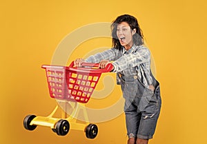 surprised woman carry shopping cart. girl in checkered shirt and jeans in shop. shopper in mall. making christmas