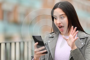 Surprised woman checking cell phone in the street