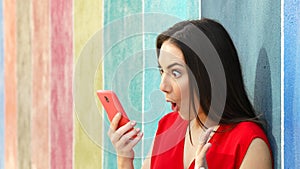 Surprised woman checking phone in a colorful wall