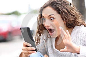 Surprised woman checking phone content in the street