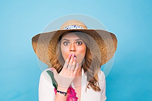Surprised woman covering her mouth with hands over blue background with copy space and looking at camera