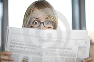 Surprised woman with glasses reading a newspaper