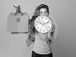 Surprised woman hiding behind clock and showing shopping bags