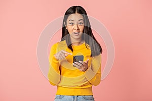 Surprised woman holding mobile phone standing on pink background. Good news, discounts or sale, online shopping