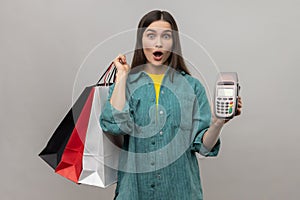 Surprised woman holding payment terminal and paper shopping bags, easy express order and delivery.