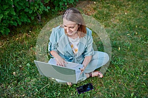 surprised woman with laptop sitting on green grass