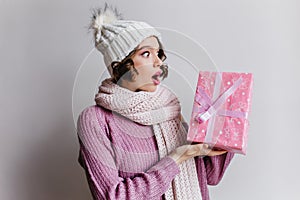 Surprised woman  on light background looking at christmas present. Indoor photo of amazed female model wears hat