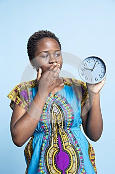 Surprised woman looking at blue round clock to check the time