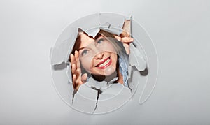 Surprised woman looking playfully in torn paper hole, has excited cheerful expression, looks through breakthrough of