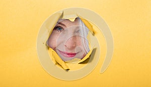 Surprised woman looking playfully in torn paper hole, has excited cheerful expression, looks through breakthrough of