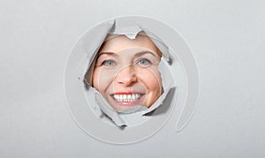 Surprised woman looking playfully in torn paper hole, has excited cheerful expression, looks through breakthrough of