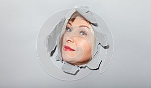 Surprised woman looking playfully in torn paper hole, has excited cheerful expression, looks through breakthrough of