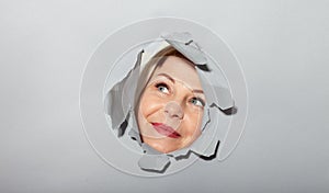 Surprised woman looking playfully in torn paper hole, has excited cheerful expression, looks through breakthrough of