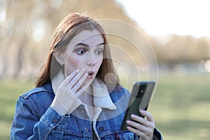 Surprised woman looks at her phone in a park in autumn