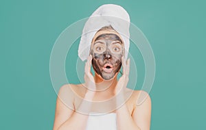 Surprised woman with mud facial mask, face clay mask spa. Beautiful woman with cosmetic mud facial procedure, spa health