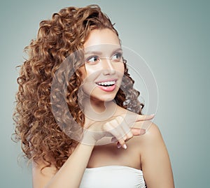Surprised woman pointing. Beautiful female model girl with long curly hair pointing to the side. Positive emotion.