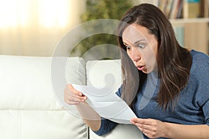 Surprised woman reading a letter on a couch at home