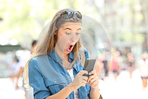 Surprised woman reading phone text in the street