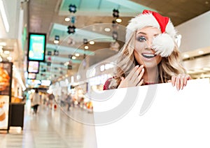 Surprised woman in Santa hat showing big white empty paper