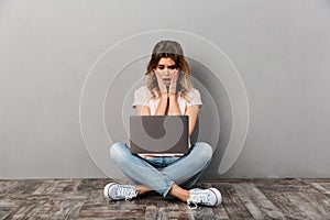 Surprised woman in t-shirt sitting on floor with laptop computer