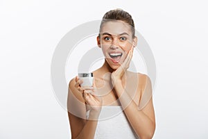 A surprised woman with a towel on her body applies a cream on the face skin.