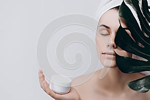 A surprised woman with a towel on her head holds a large green leaf and Cream for Face.