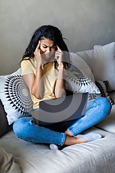 Surprised woman using smart phone and laptop sitting on a couch in the living room at home