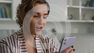 Surprised woman using smartphone reading messages in pajamas at home closeup.