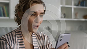 Surprised woman using smartphone reading messages in pajamas at home closeup.