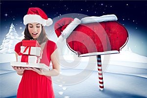 Surprised woman wearing santa hat holding stack of gifts