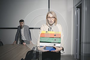 Surprised woman and bearded man on background. Business woman in glasses hold file folders. secretary with office